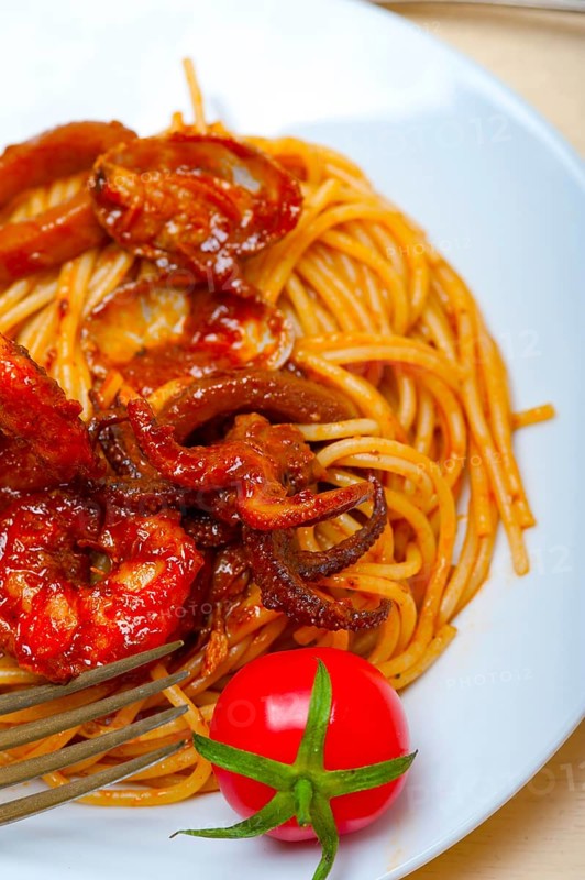 Italian seafood spaghetti pasta on red tomato sauce over white rustic wood table