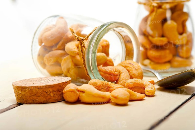 Cashew nuts on a glass jar over white rustic wood table