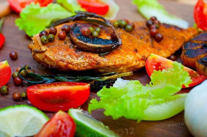 Wood fired hoven cooked chicken breast on wood board with herbs spices and vegetables
