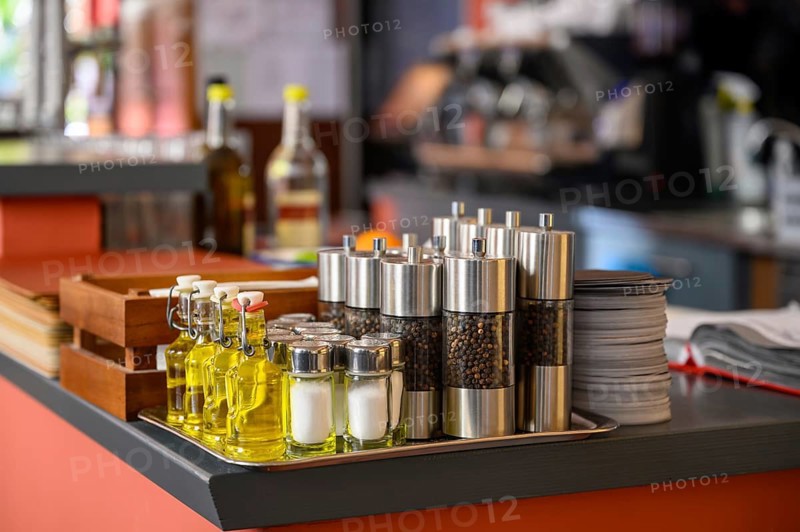 Salt and pepper shakers and small bottles of olive oil are placed on the counter of a restaurant