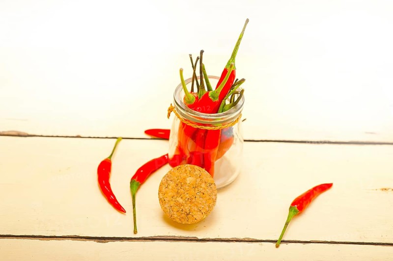 Red chili peppers on a glass jar over white wood rustic table