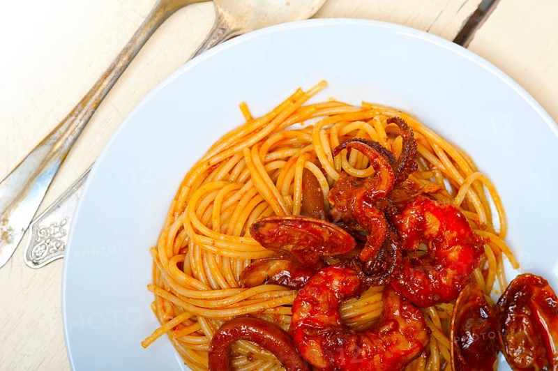Italian seafood spaghetti pasta on red tomato sauce over white rustic wood table