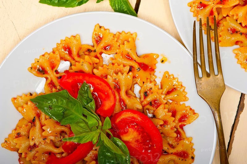 Italian pasta farfalle butterfly bow-tie with tomato basil sauce over white rustic wood table