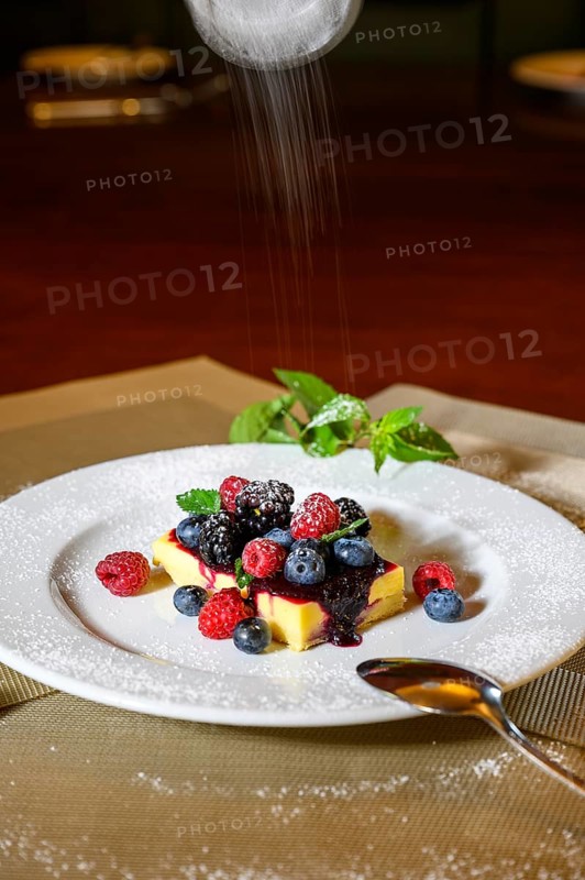 A slice of cheesecake with fresh raspberries and blackberries and a layer of icing sugar on a white plate