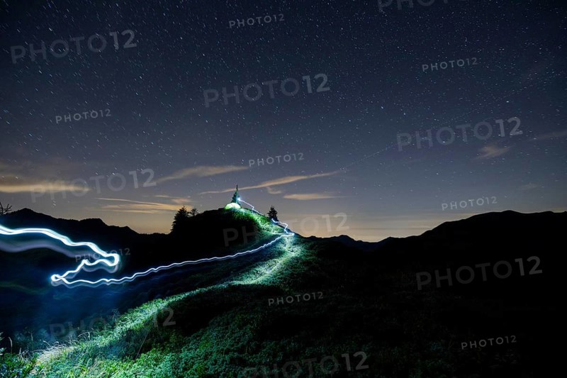 Green tent and tracer with headlamp under a starry sky on the Portlakopf