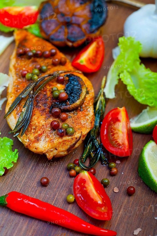Wood fired hoven cooked chicken breast on wood board with herbs spices and vegetables