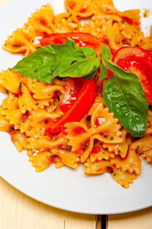 Italian pasta farfalle butterfly bow-tie with tomato basil sauce over white rustic wood table