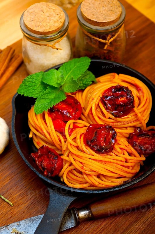 Italian spaghetti pasta and tomato with mint leaves on iron skillet over wood board
