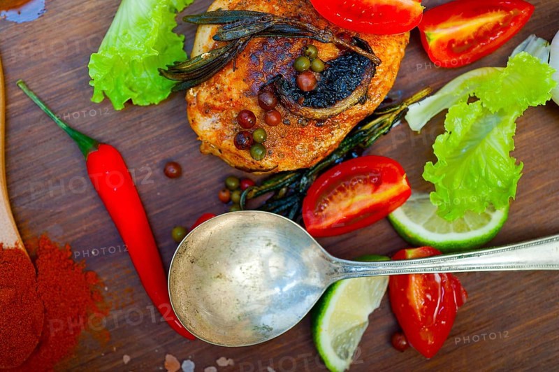 Wood fired hoven cooked chicken breast on wood board with herbs spices and vegetables