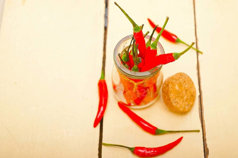 Red chili peppers on a glass jar over white wood rustic table