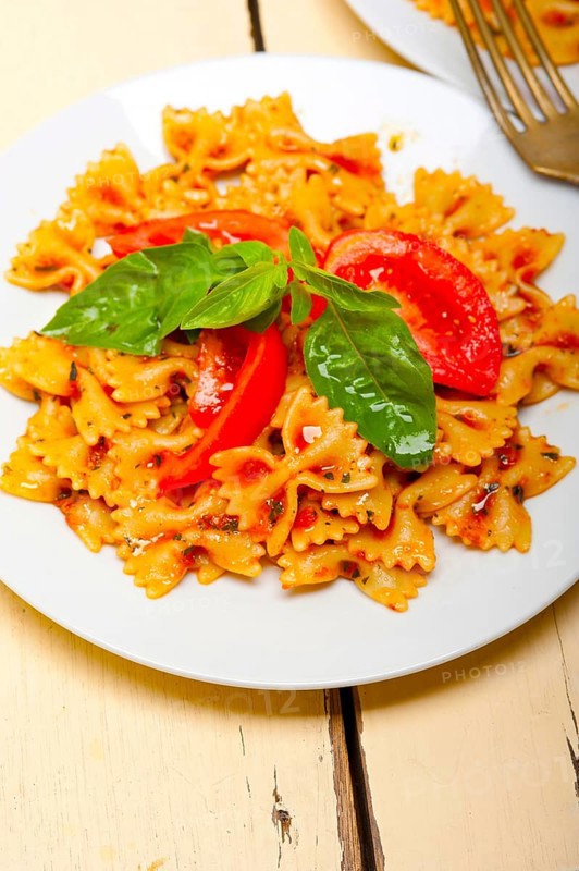 Italian pasta farfalle butterfly bow-tie with tomato basil sauce over white rustic wood table