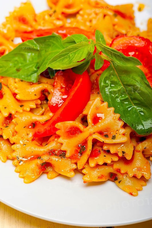 Italian pasta farfalle butterfly bow-tie with tomato basil sauce over white rustic wood table
