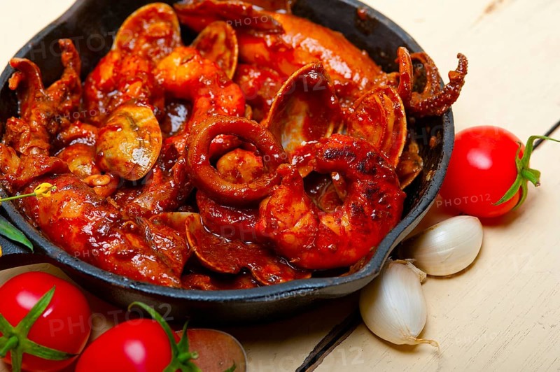 Fresh seafood stew prepared on an iron skillet ove white rustic wood table