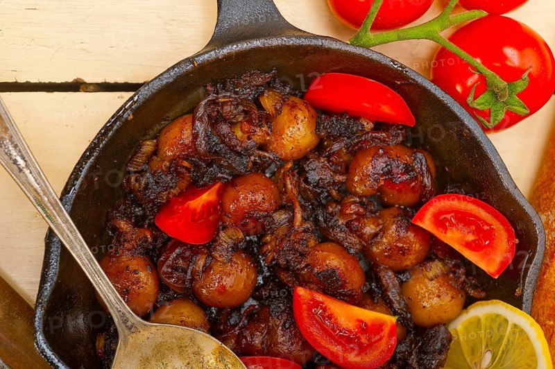 Baby cuttle fish roasted on iron skillet with tomatoes and onions over rustic wood table