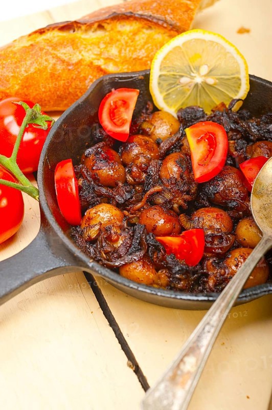 Baby cuttle fish roasted on iron skillet with tomatoes and onions over rustic wood table