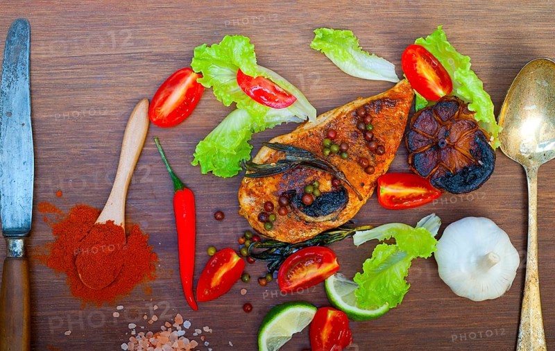 Wood fired hoven cooked chicken breast on wood board with herbs spices and vegetables