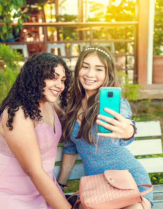 Two pretty girls sitting on a bench taking a selfie