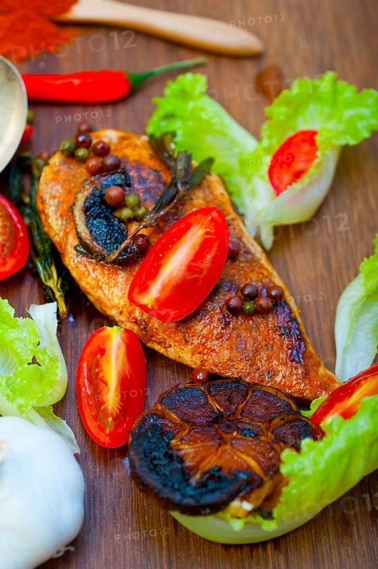 Wood fired hoven cooked chicken breast on wood board with herbs spices and vegetables