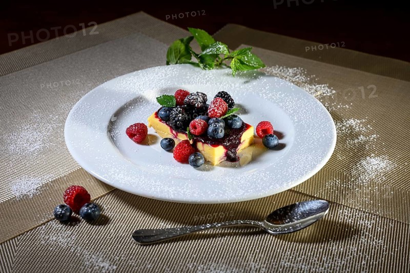 A slice of cheesecake with fresh raspberries and blackberries and a layer of icing sugar on a white plate