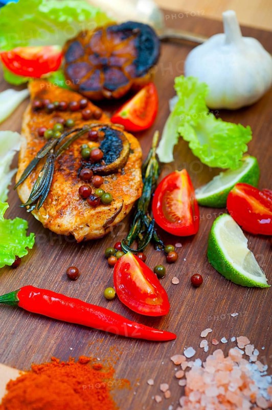 Wood fired hoven cooked chicken breast on wood board with herbs spices and vegetables