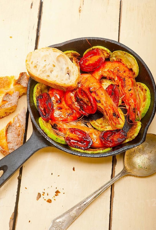 Roasted shrimps on cast iron skillet with zucchini and tomatoes