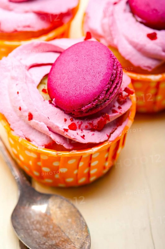 Fresh pink berry cream cupcake with macaroon on top over rustic wood table