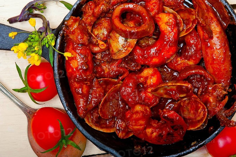 Fresh seafood stew prepared on an iron skillet ove white rustic wood table