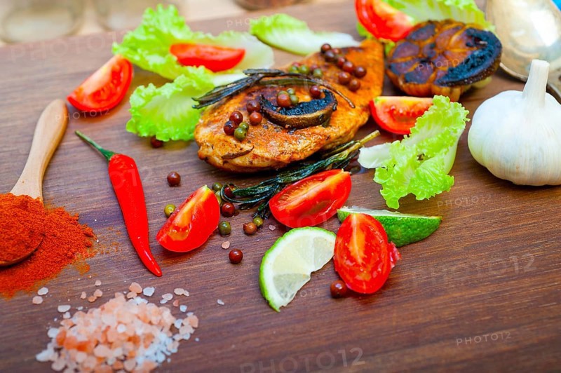 Wood fired hoven cooked chicken breast on wood board with herbs spices and vegetables