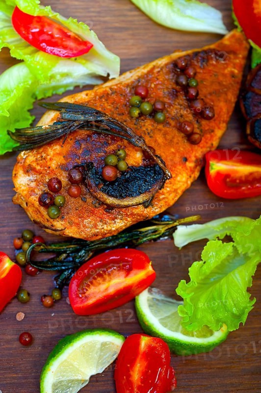Wood fired hoven cooked chicken breast on wood board with herbs spices and vegetables