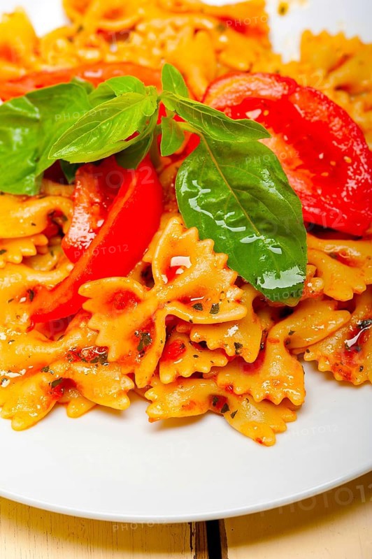 Italian pasta farfalle butterfly bow-tie with tomato basil sauce over white rustic wood table