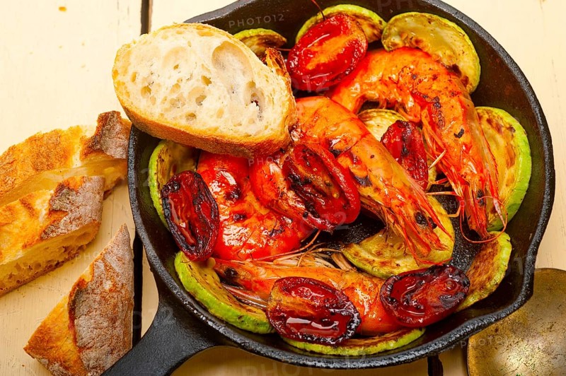 Roasted shrimps on cast iron skillet with zucchini and tomatoes