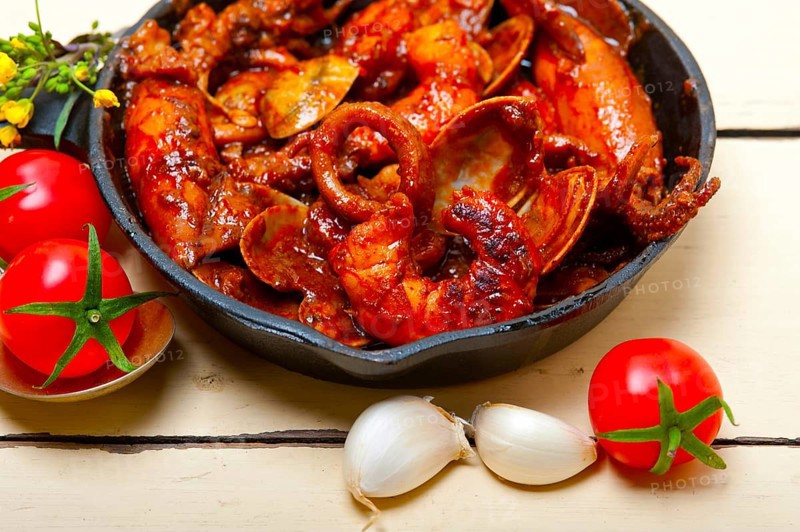 Fresh seafood stew prepared on an iron skillet ove white rustic wood table