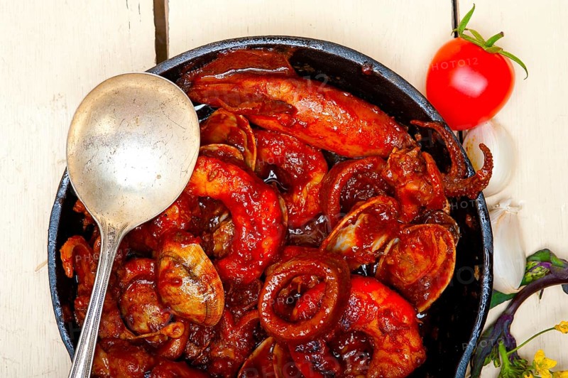 Fresh seafood stew prepared on an iron skillet ove white rustic wood table