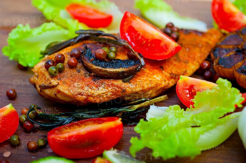 Wood fired hoven cooked chicken breast on wood board with herbs spices and vegetables