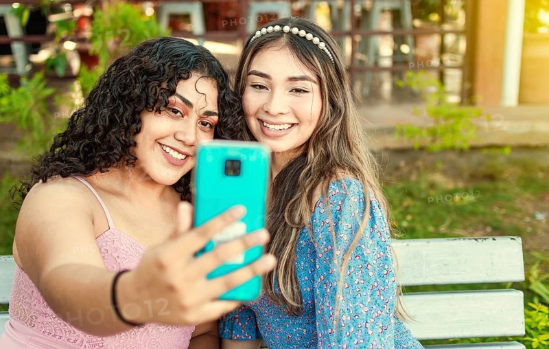 Two pretty girls sitting on a bench taking a selfie