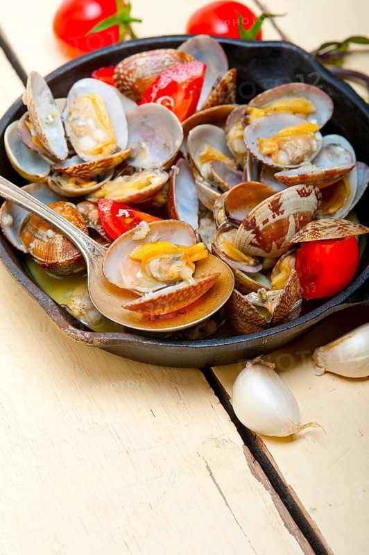 Fresh clams stewed on an iron skillet over wite rustic wood table
