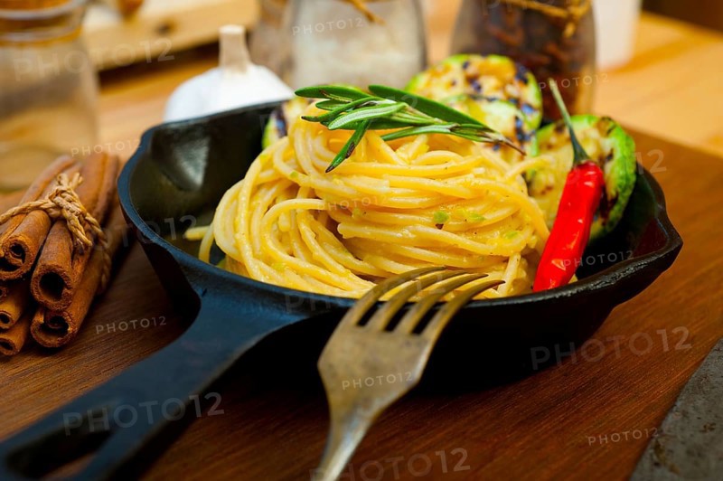 Italian spaghetti pasta with zucchini sauce on iron skillet over wood board