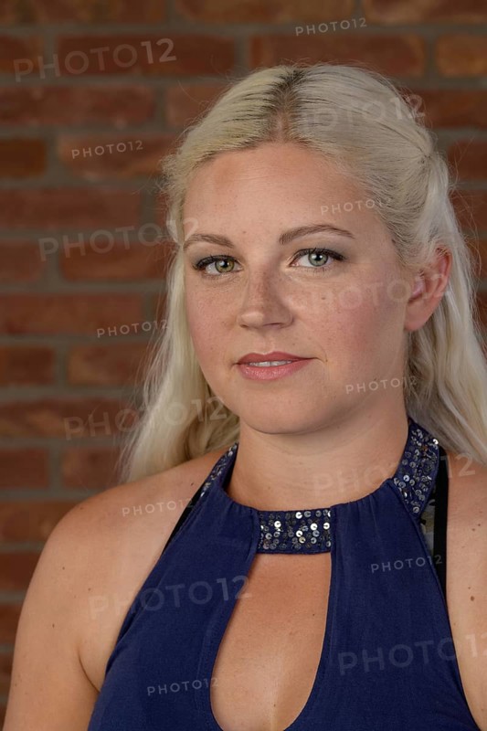 Pretty young woman with freckles and long blond hair in a sleeveless dress in front of a red brick wall