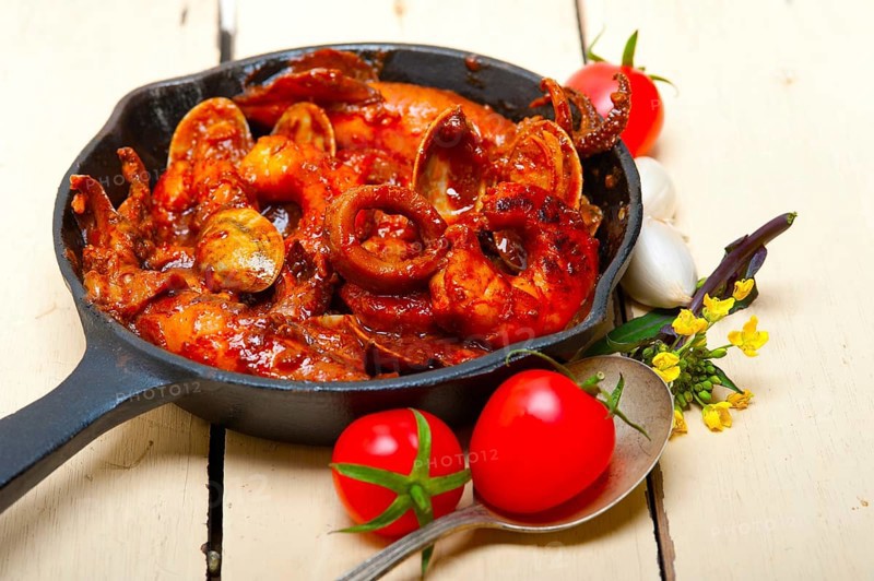 Fresh seafood stew prepared on an iron skillet ove white rustic wood table