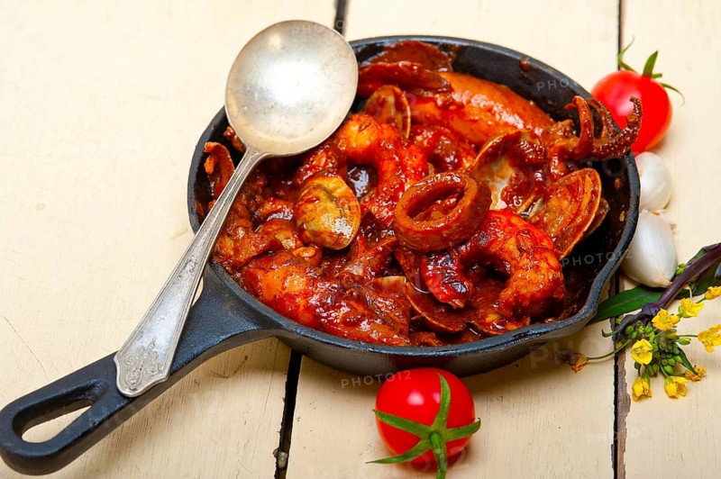 Fresh seafood stew prepared on an iron skillet ove white rustic wood table
