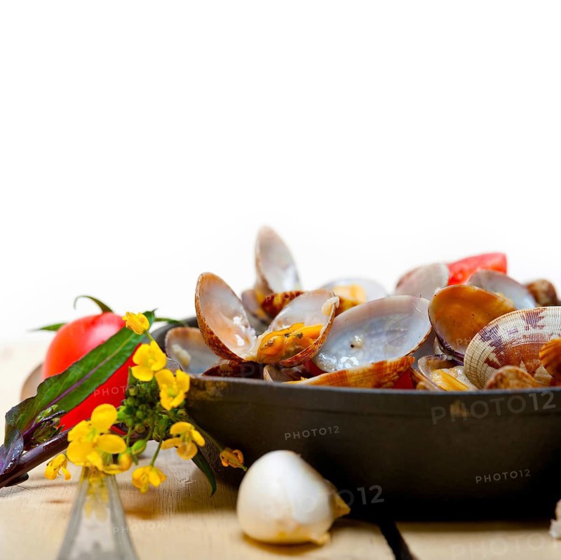 Fresh clams stewed on an iron skillet over wite rustic wood table
