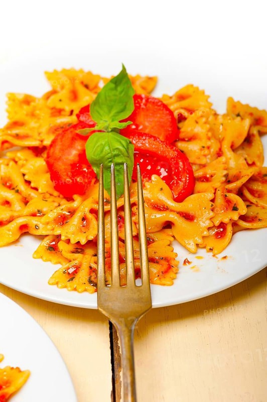 Italian pasta farfalle butterfly bow-tie with tomato basil sauce over white rustic wood table