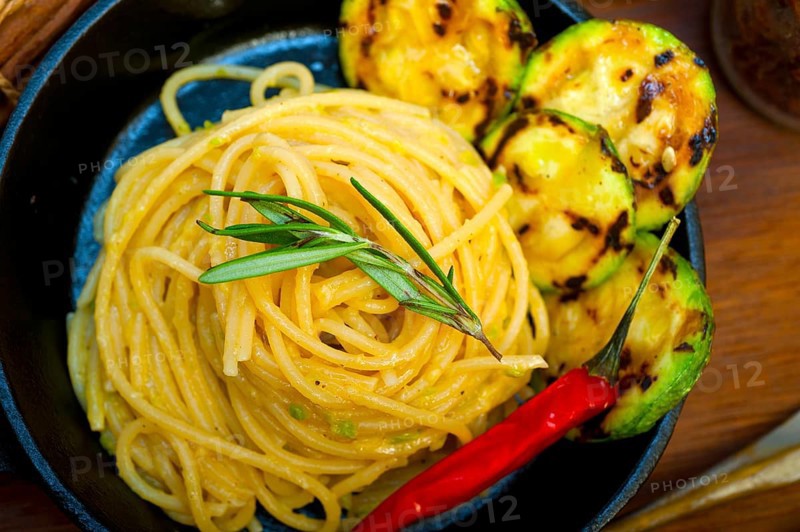 Italian spaghetti pasta with zucchini sauce on iron skillet over wood board