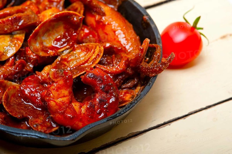 Fresh seafood stew prepared on an iron skillet ove white rustic wood table