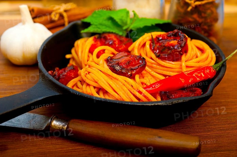 Italian spaghetti pasta and tomato with mint leaves on iron skillet over wood board