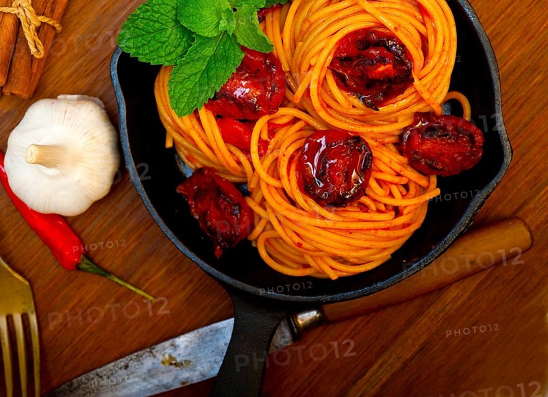 Italian spaghetti pasta and tomato with mint leaves on iron skillet over wood board
