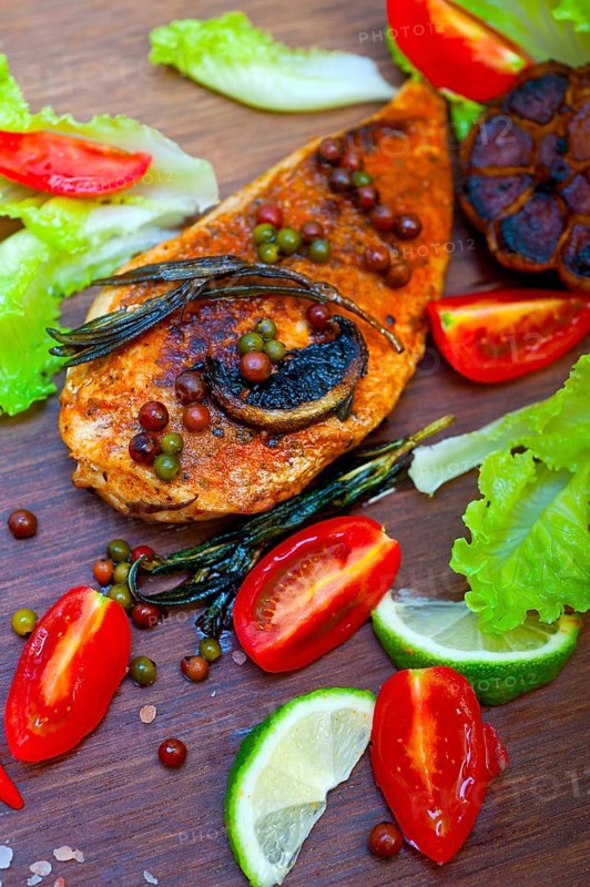 Wood fired hoven cooked chicken breast on wood board with herbs spices and vegetables