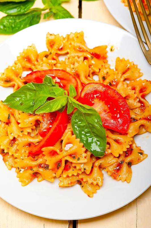 Italian pasta farfalle butterfly bow-tie with tomato basil sauce over white rustic wood table