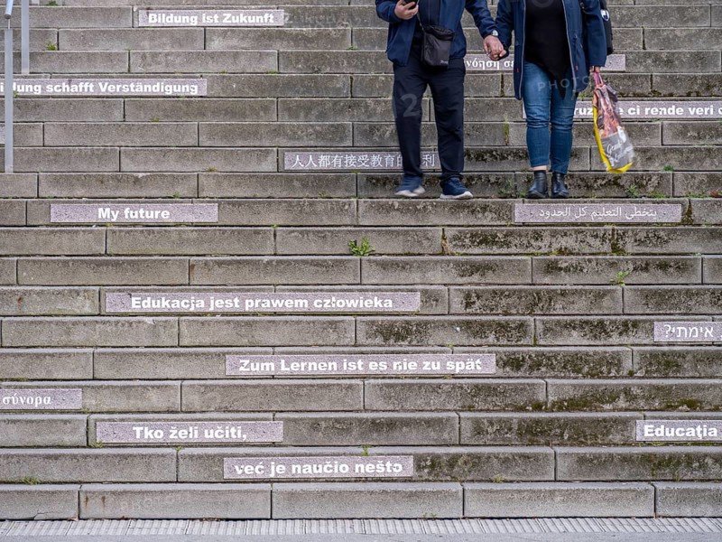 A couple walking down stairs with slogans about education and learning in several languages