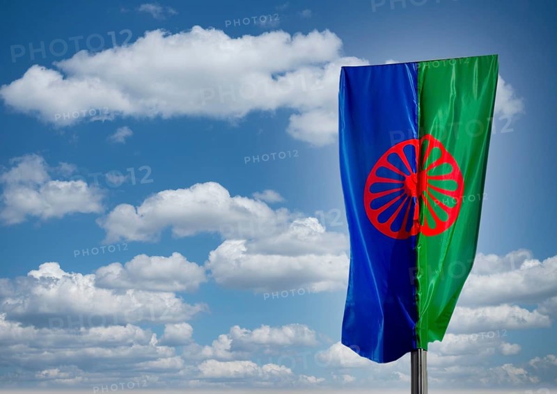 Eine Roma und Sintiflagge weht im Wind mit Wolken als Hintergrund